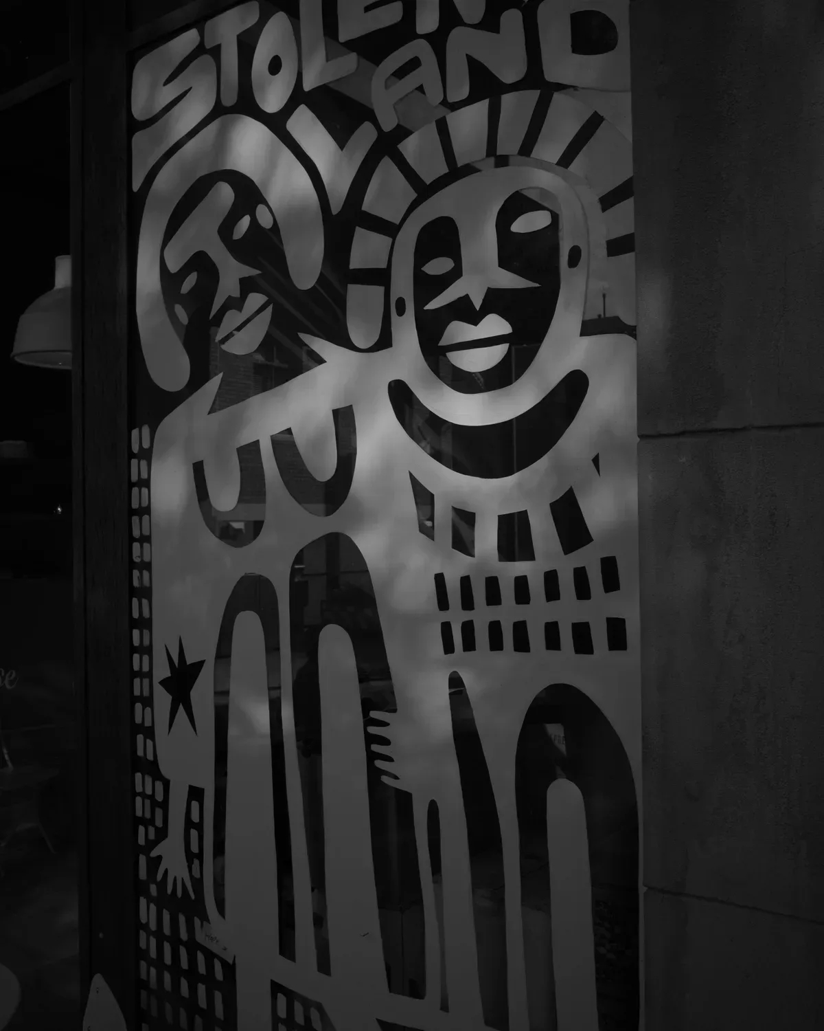 A window mural reading STOLEN LAND, with two smiling figures in bold black and white lines.