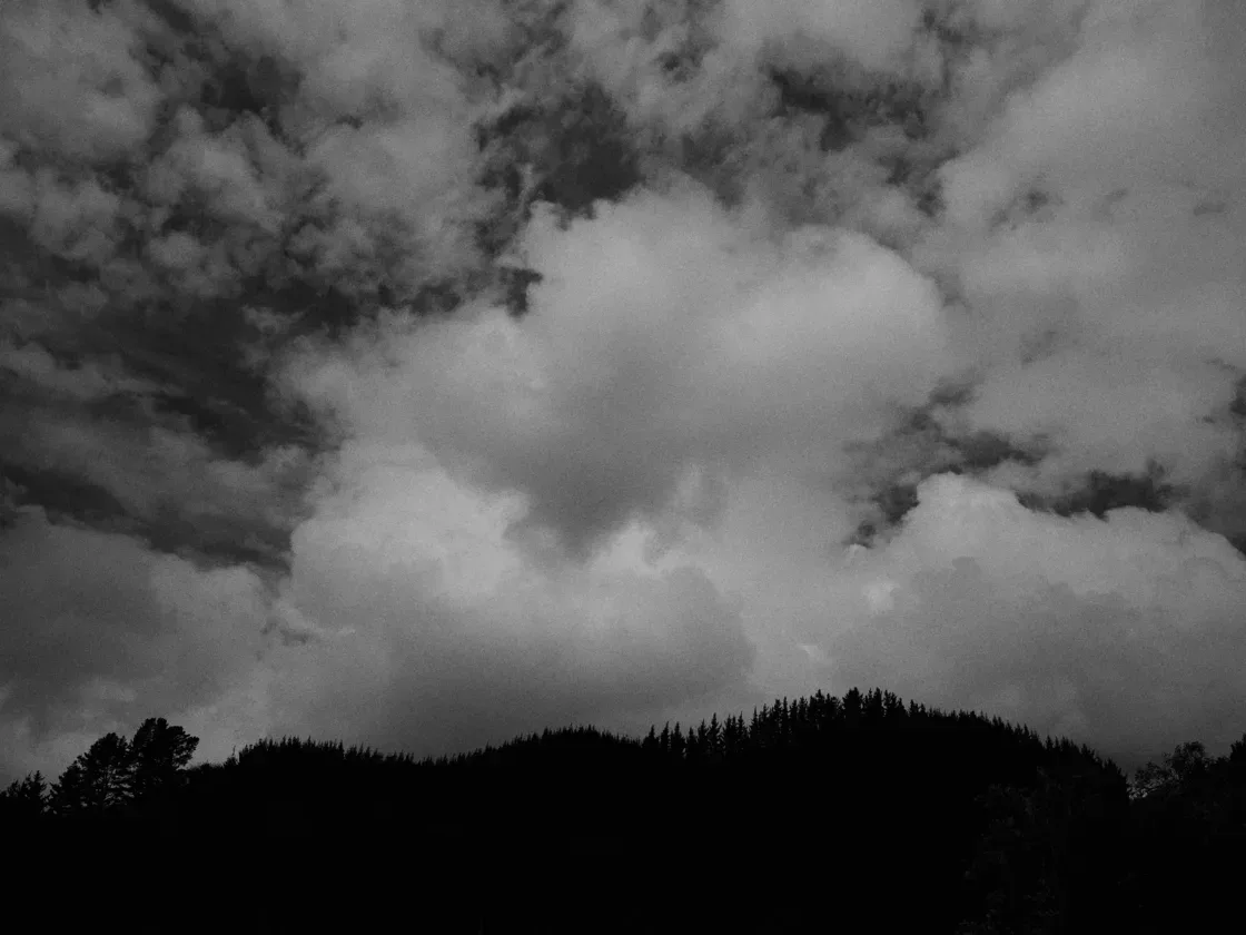 Heavy storm clouds over a dark, forested ridgeline.